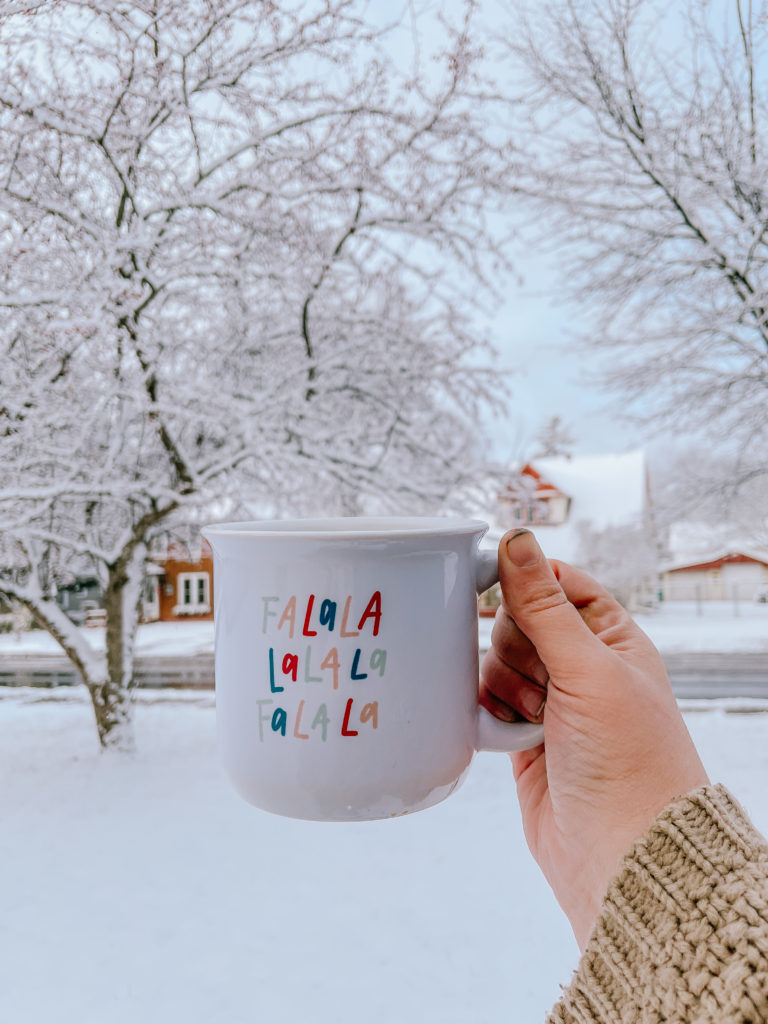 Fa La La La coffee mug in front of a snowy front yard.