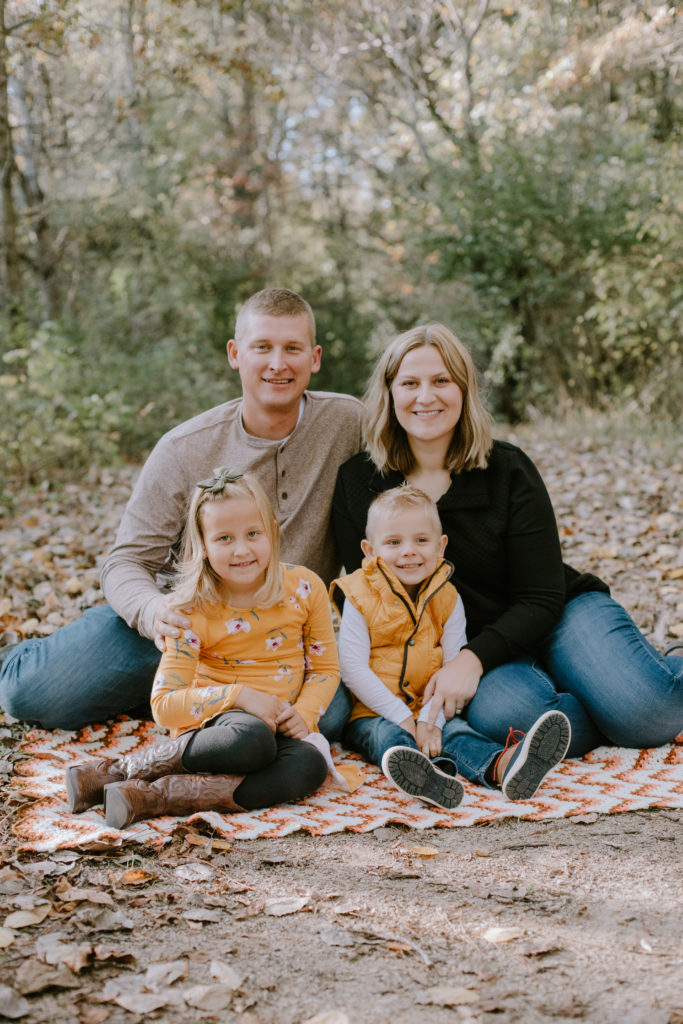 Family sitting on a blanket in the woods during their fall mini session.