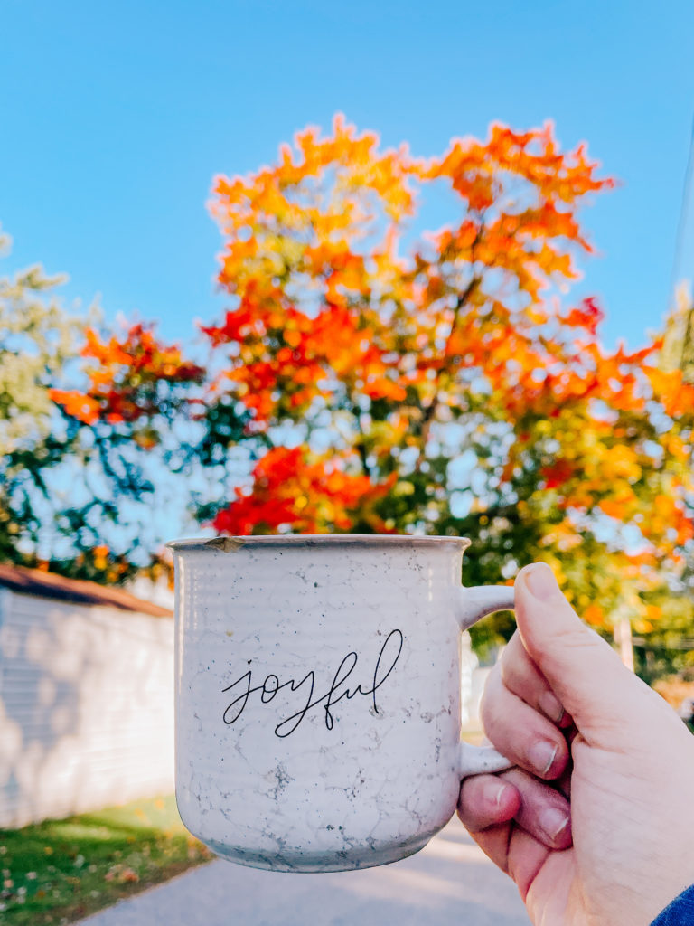 Coffee cup in front of fall trees in morning light, behind the scenes