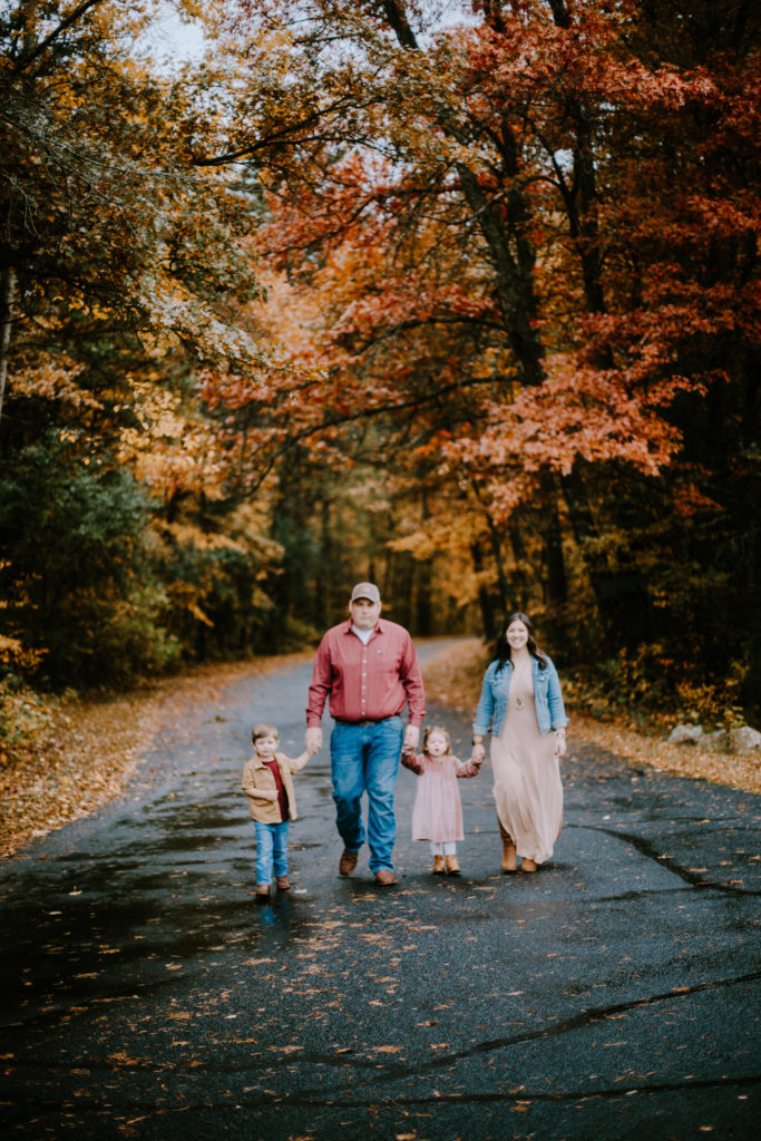 Family with a little boy and little girl walking down a street lined with fall foliage at their Stevens Point family session.