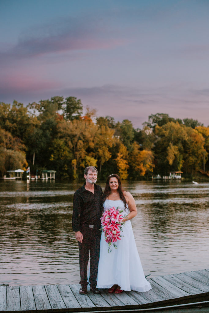 Bride and groom standing on the dock overlooking a gorgeous pink sunset during their Appleton Yacht Club wedding day.