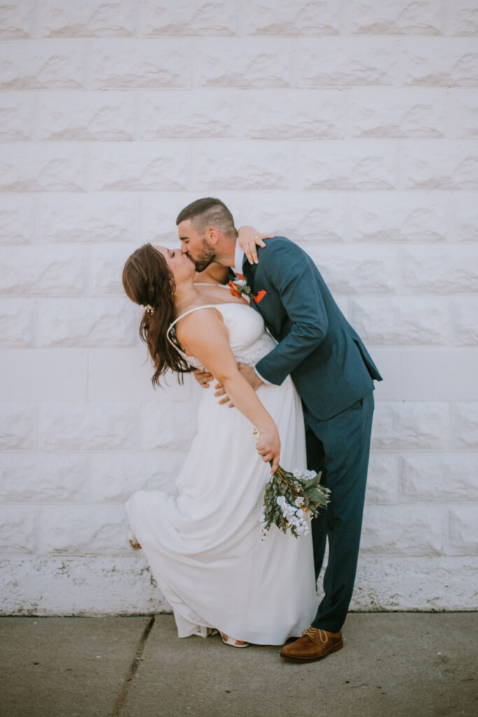 Bride and groom kiss in front of a white brick wall during their Mercantile Hall wedding day