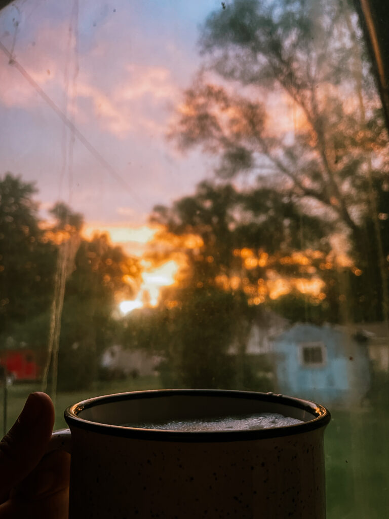 Currently: Gorgeous golden sunrise out a dirty window with a cup of coffee in the foreground.