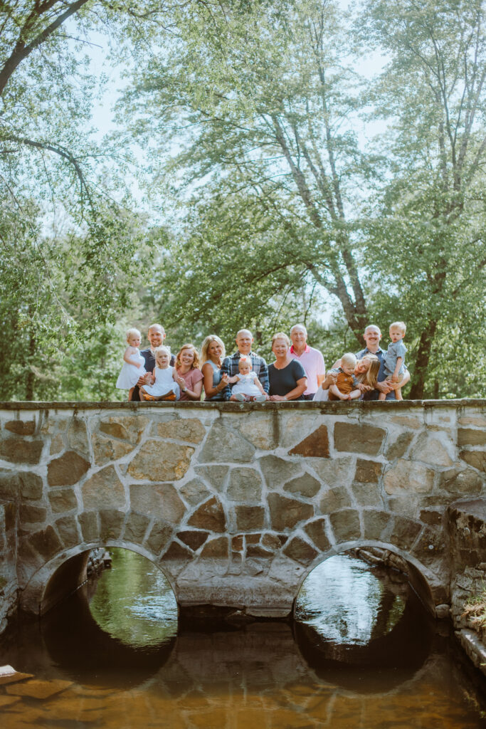 Three generations (grandparents, siblings, and grandchildren) standing on a bridge during their extended family session at Iverson Park in Stevens Point.