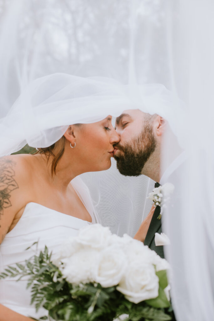 Couple kissing under the bride's veil during their Danes Hall wedding in Waupaca, WI.
