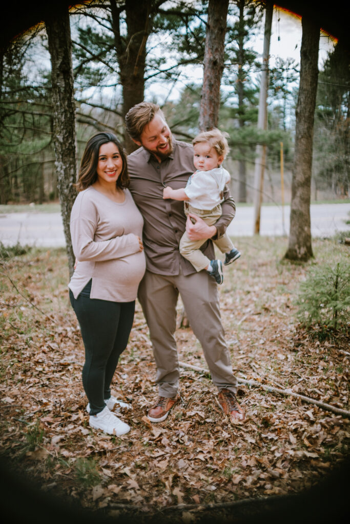 Pregnant mama, dad, and toddler smile at the camera during their Oakwood Park family session on the Waupaca Chain O' Lakes in King, WI.