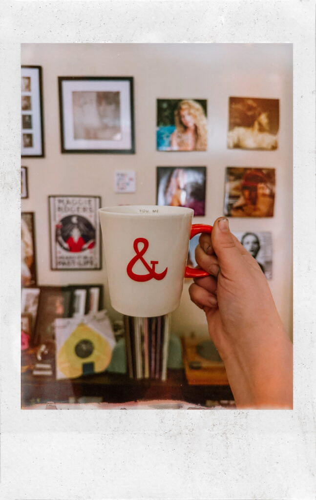 Currently, a coffee cup being held in front of a wall of Taylor Swift vinyl.