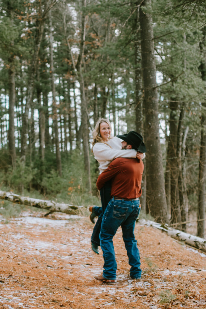 Couple spins around in the snow covered forest during their engagement session at Hartman Creek State Park in Waupaca, WI.