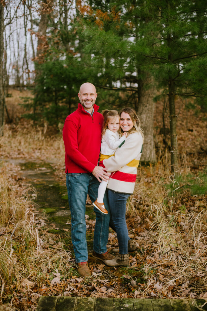 Mom, dad, and daughter standing in the woods during their family session on Stratton Lake in Waupaca, WI.