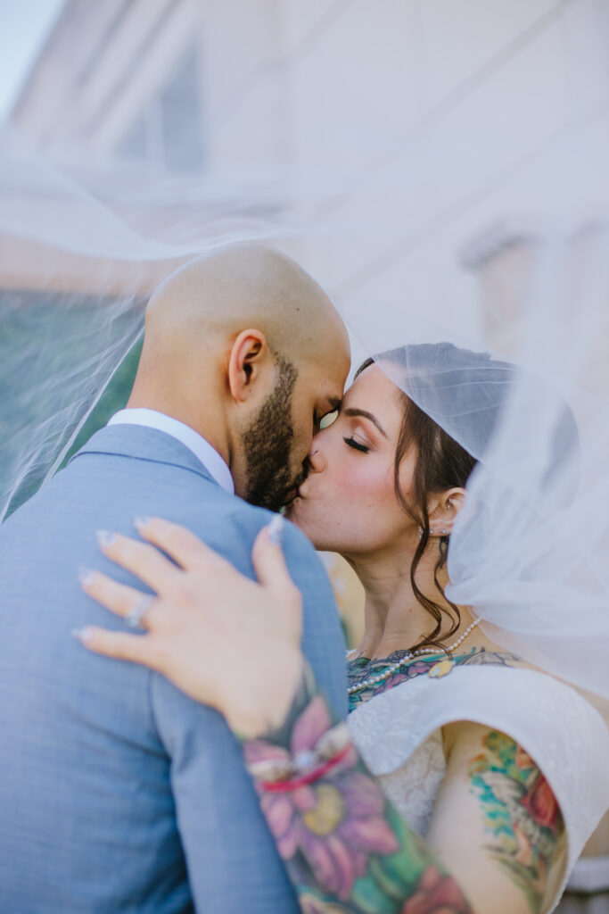 Bride with colorful tattoos and groom kissing under the veil during their wedding day at Saranellos in the Westin Chicago North Shore Hotel in Wheeling, IL.