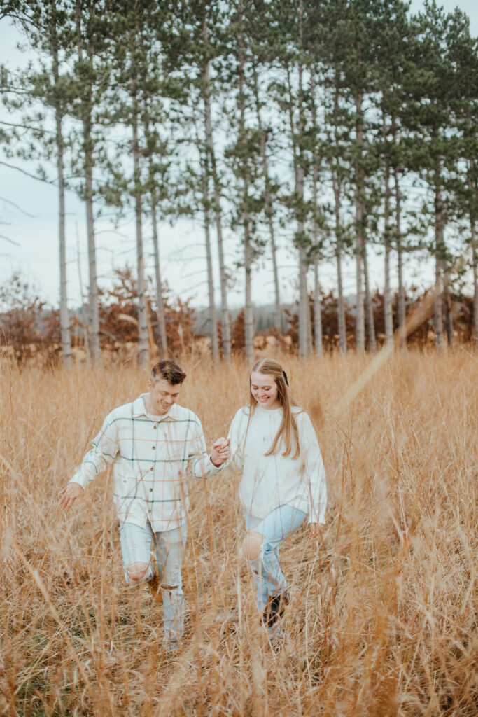 Couple frolicking through a field of tall grass during their engagement session at Emmons Creek in Waupaca, WI.