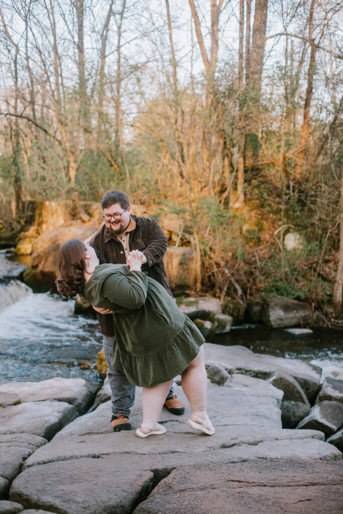 Couple does a dip on the rocks in front of the waterfall at Jordan Park in Stevens Point, WI during their engagement session.