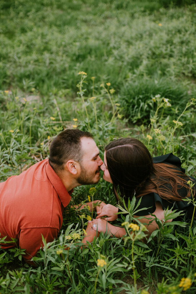 Couple laying in long grass and kissing during their spring prairie engagement session at Jorgens Park Preserve in Scandinavia, WI.