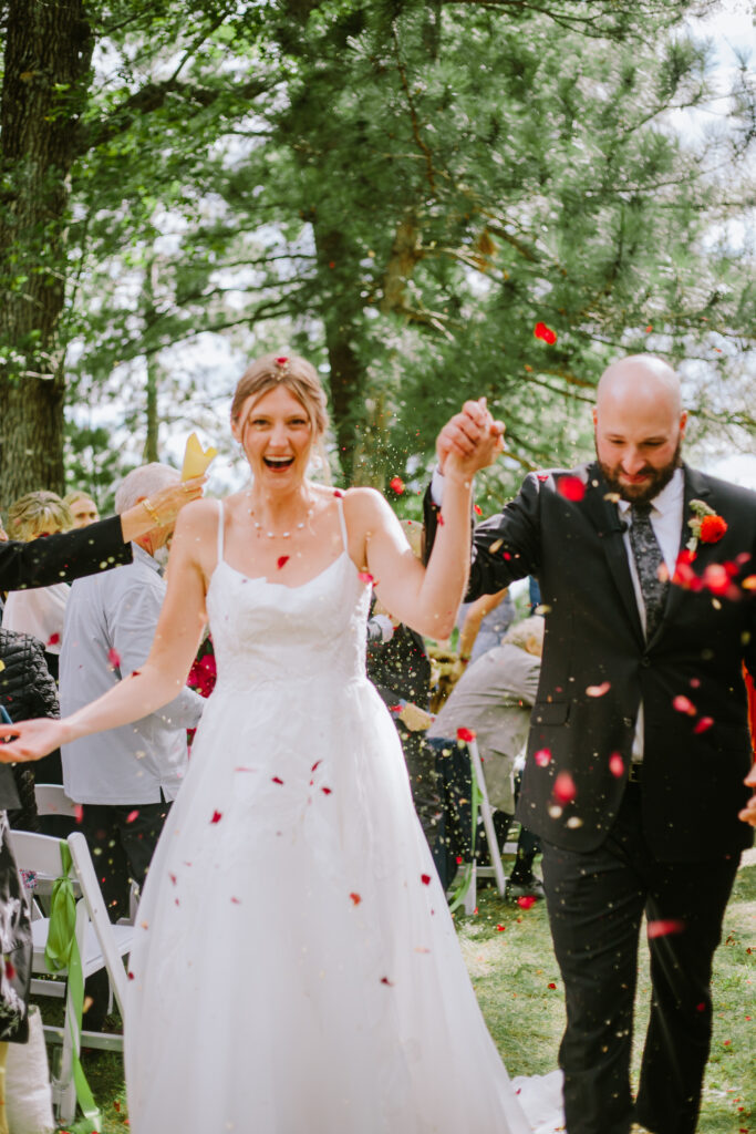 Bride and groom coming back up the aisle while being showered with red rose petals during their backyard wedding on Round Lake in the Chain O' Lakes in Waupaca, WI.